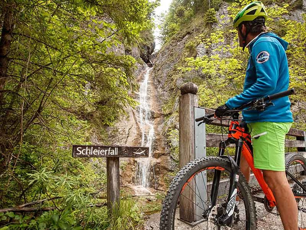 Mountainbiker hält Rast vor einem Wasserfall in den Bergen
