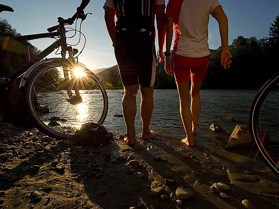 zwei Radfahrer am Ufer der Drau bei Sonnenuntergang