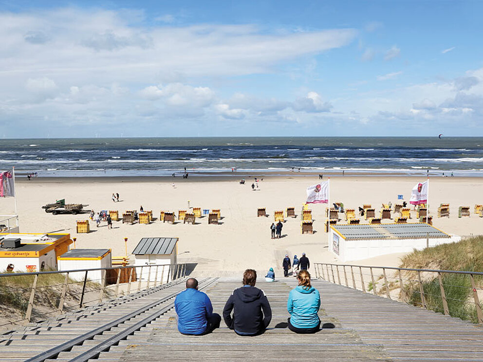 3 Personen sitzen am Strandeingang