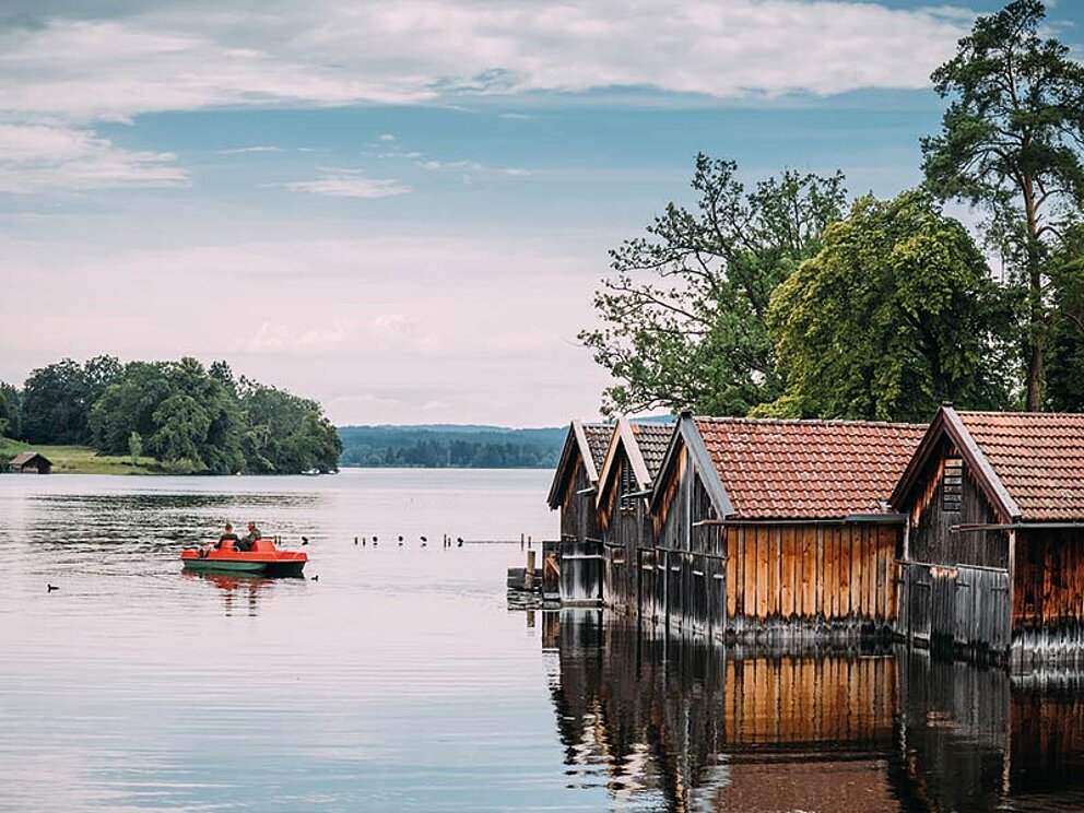 Blick auf den See mit Bootshäusern und Tretbooten