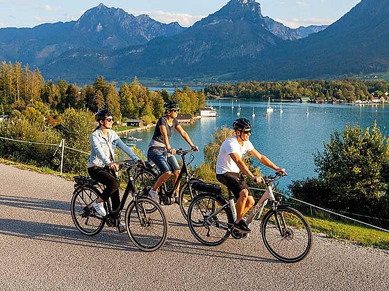 3 Radfahrer am asphaltierten Radweg am Wolfgangsee, im Hintergrund herrliches Bergpanorama