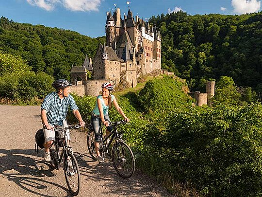 2 Radfahrer am asphaltieren Radweg, im Hintergrund die Burg Eltz