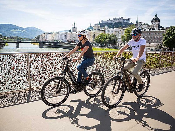 a couple rides on their bikes over Salzach bridge at Salzburg