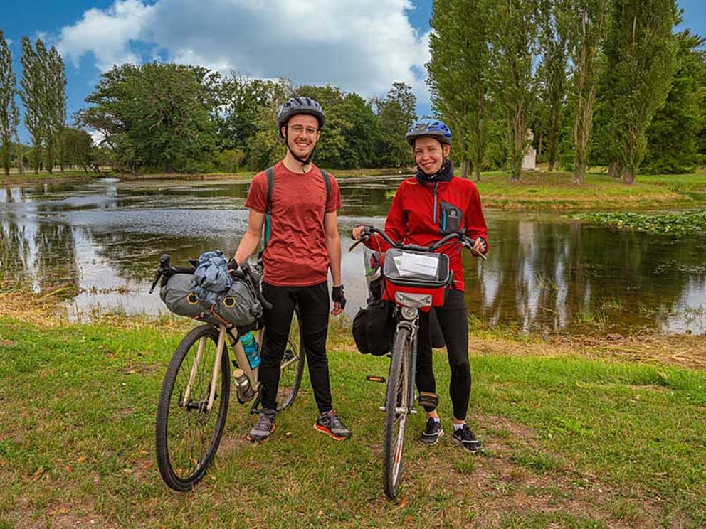 2 Radfahrer stehen mit ihren Rädern im Wörlitzer Park in Wittenberg. Dahinter die Elbe.