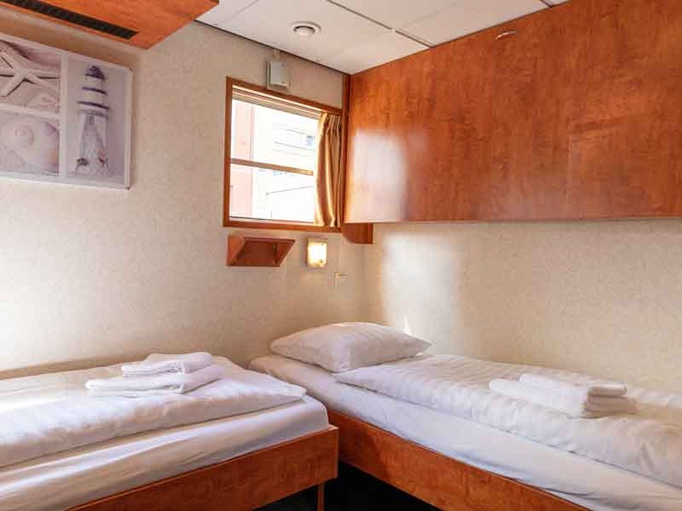 Kabine mit 2 Einzelbetten, im L angeordnet, darüber ein kleines Fenster und ein Hängeschrank
