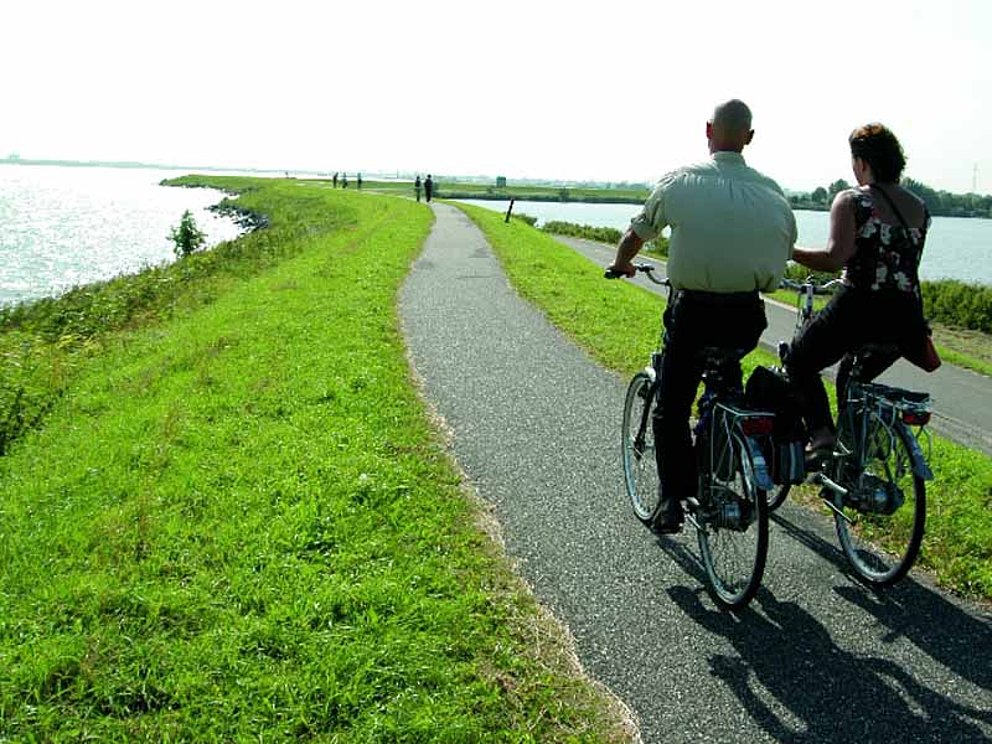 Radfahrer auf einem Damm in Holland, mit dem Meer links und rechts davon.