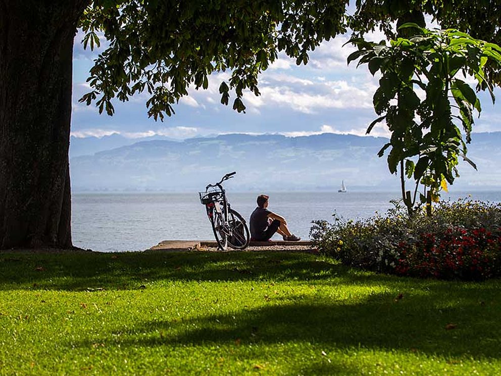cyclists sits at the lakeside  of Lake Constance, bike behind him