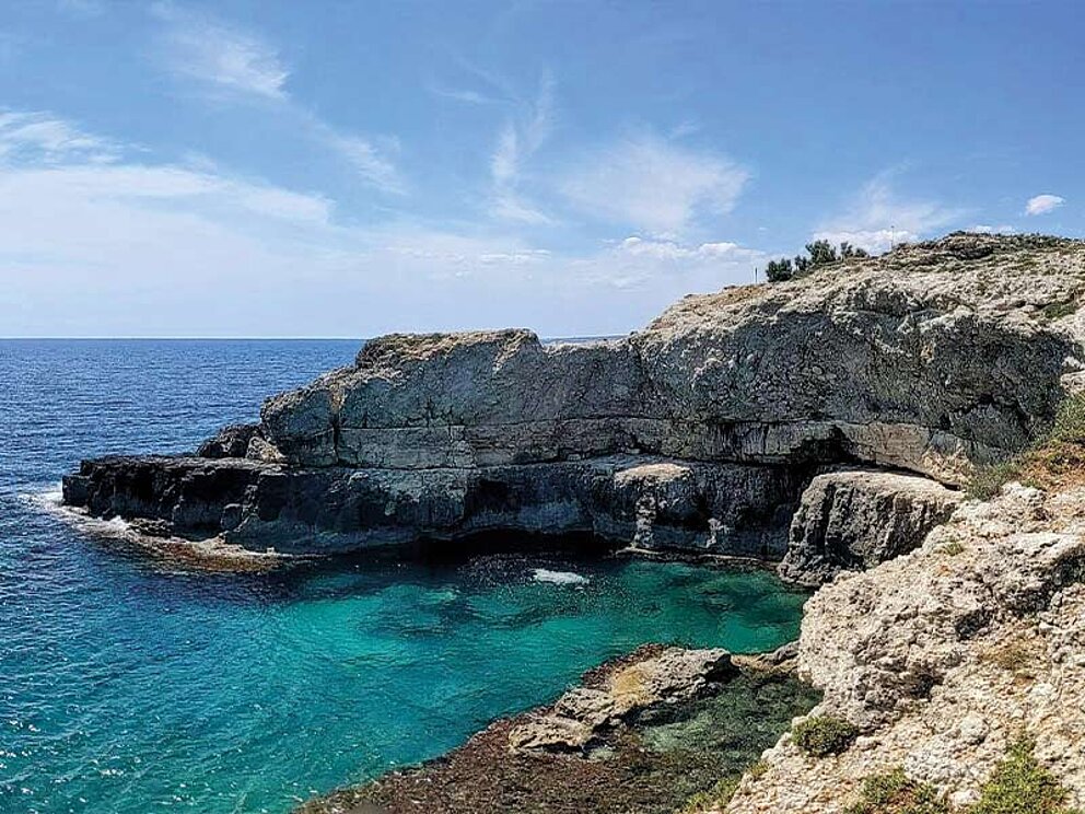 Spektakuläre Ansicht der zerklüfteten Küste Apuliens mit leuchtend türkisfarbenem Wasser in einer kleinen Bucht unter strahlend blauem Himmel.