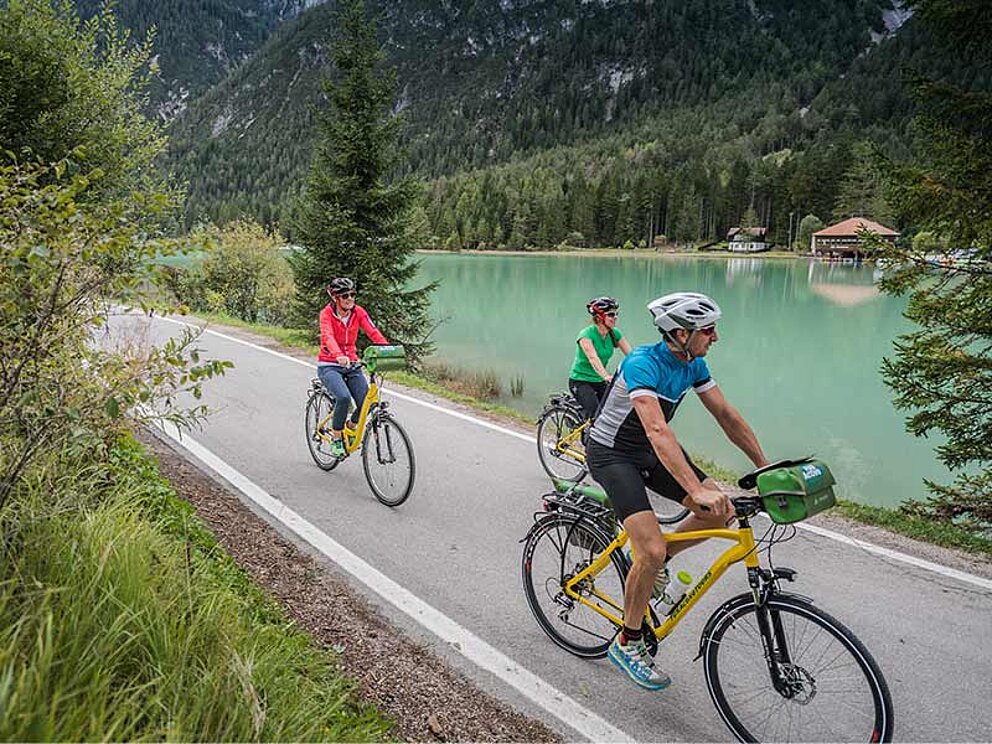 3 Radfahrer am asphaltierten Radweg am Ufer eines Sees
