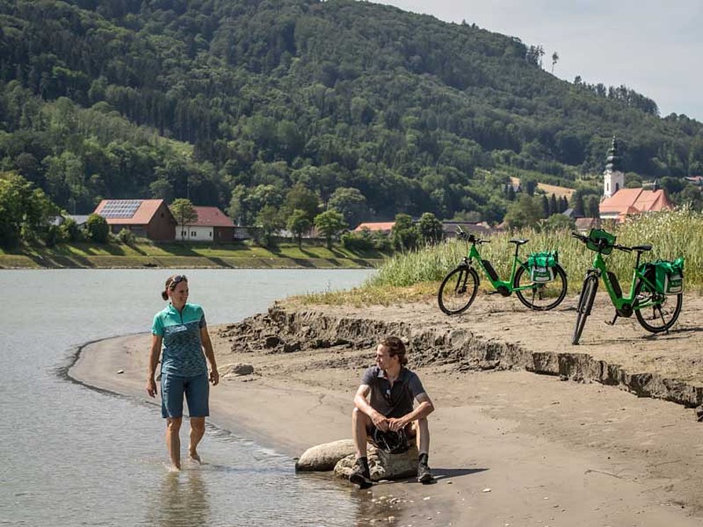 Radfahrer steht bis zu den Knöcheln in der Donau, Rast am Ufer