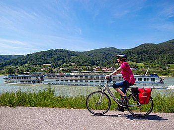 1 Radfahrer am Radweg, im Hintergrund die Donau mit der MS Swiss Crown