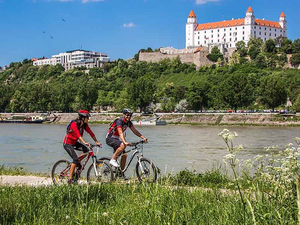 zwei Radfahrer unterwegs am Donauradweg vorbei an der Burg in Bratislava