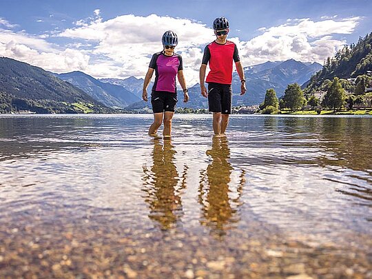 2 Personen in Radkleidung kühlen ihre Beine im Zeller See ab.