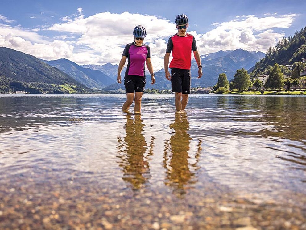 2 Personen in Radkleidung kühlen ihre Beine im Zeller See ab.