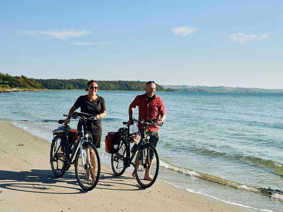 Radfahrer schieben ihre Räder am Sandstrand in Dänemark