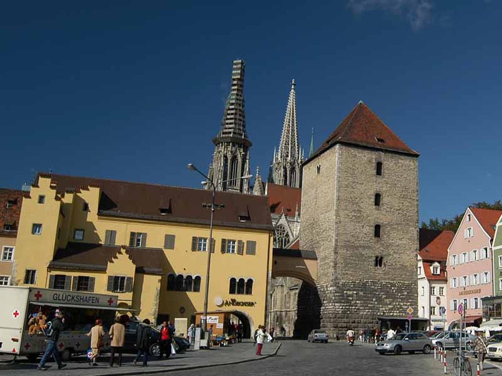 Das historische Stadttor in Regensburg macht den Durchlass in die Stadt frei. Dahinter ragen die Türme des Domes in die Höhe.