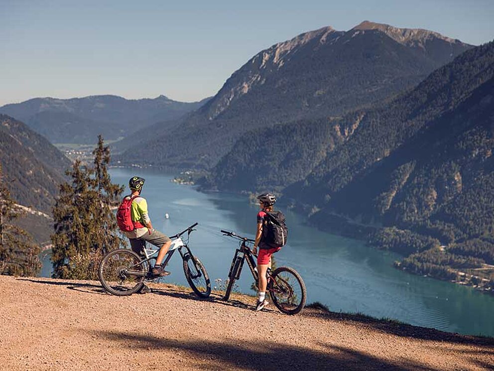 2 Mountainbiker stehen an einer Bergkante und blicken auf den Achensee hinab.