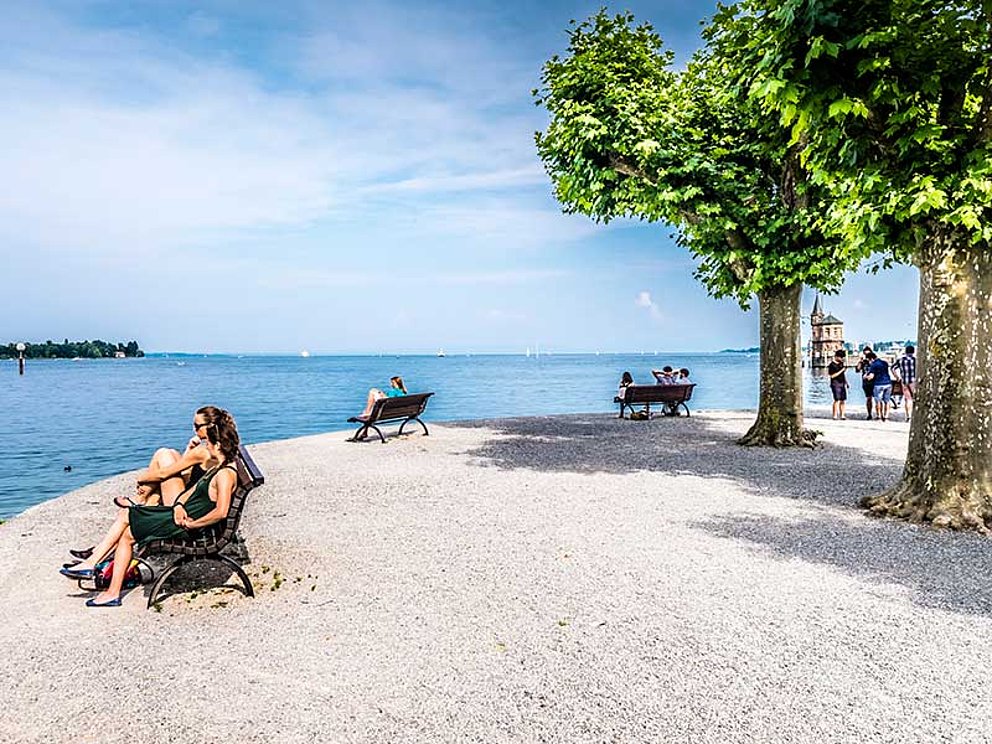 a couple sits on a bench at the lakeside of Lake Constance