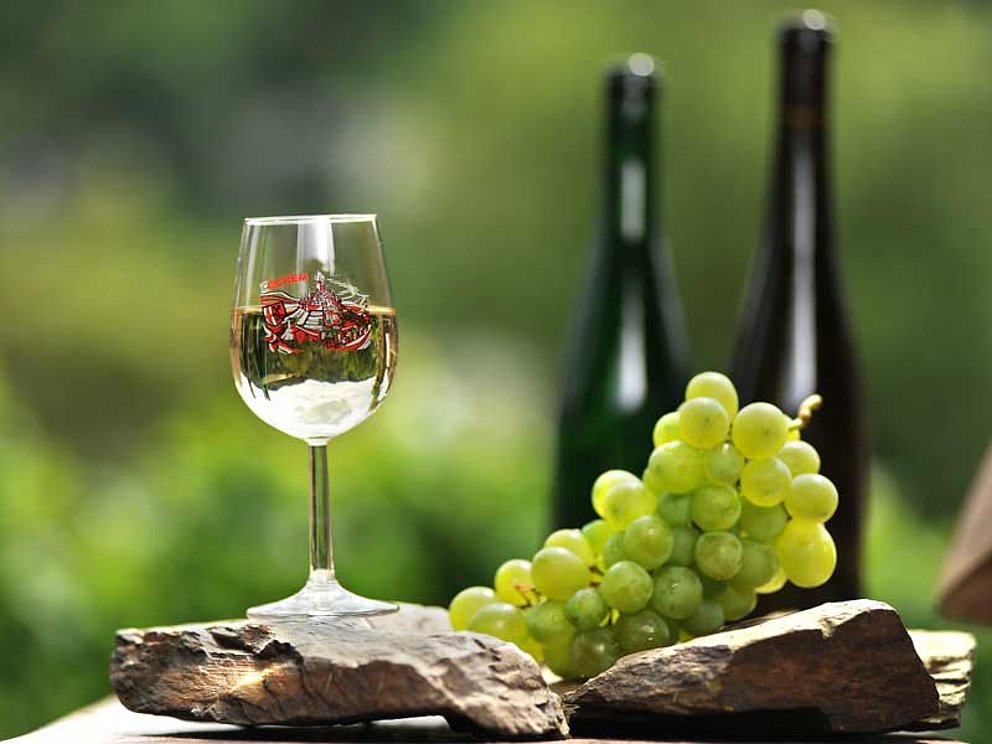 2 Flaschen Moselwein, 1 halbgefülltes Glas Weißwein, Weintrauben und Steine