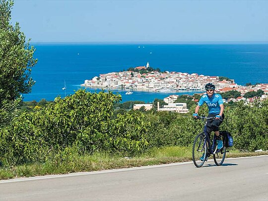 Ein Radfahrer auf einer Straße, im Hintergrund eine Halbinsel umgeben von Meer