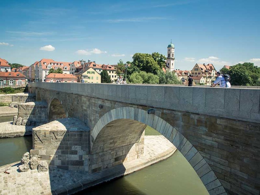 Ein Radfahrer fährt über die Steinerne Brücke auf die historische Altstadt von Regensburg zu.