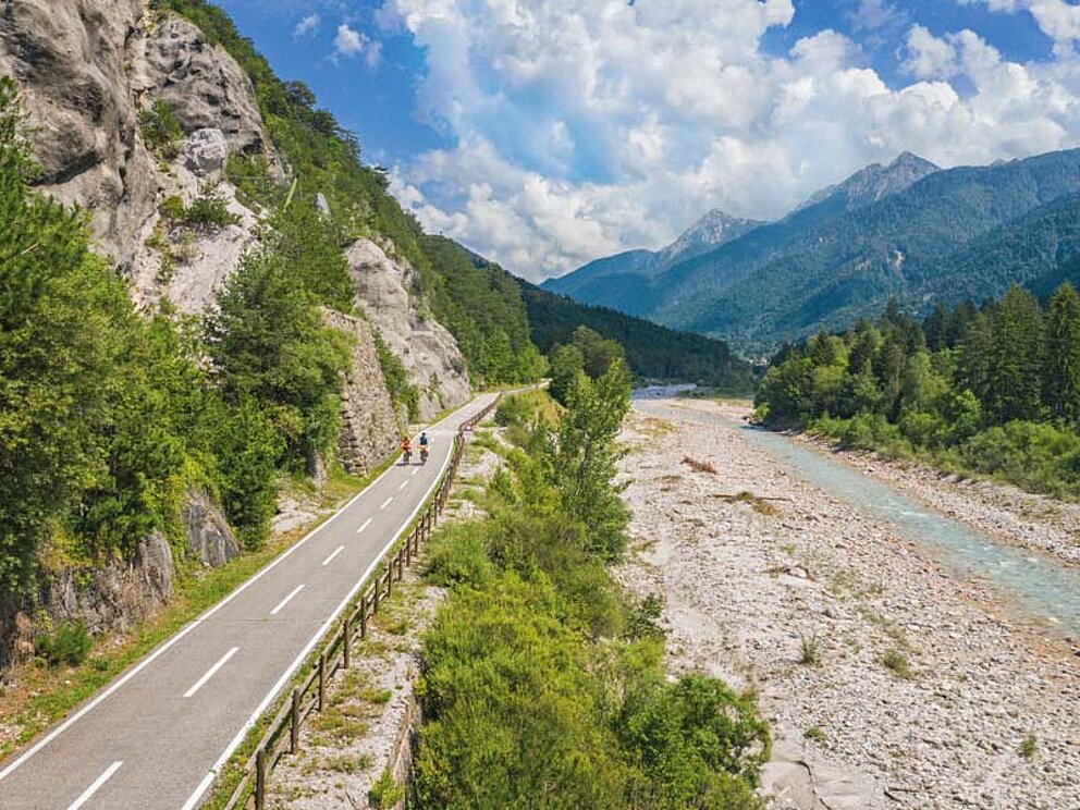 Kanaltal mit Fluss, einem Radweg und Bergpanorama
