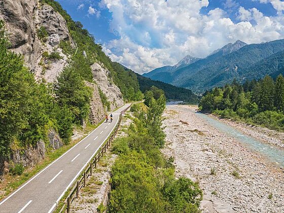 Kanaltal mit Fluss, einem Radweg und Bergpanorama