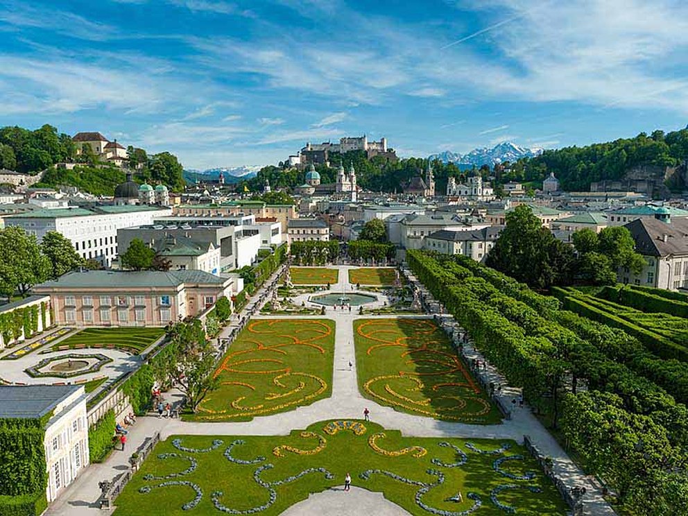Die gepflegte Parkanlage des Mirabellgartens in Salzburg. Der Garten ist barock angelegt, mit breiten Wegen, Springbrunnen, Blumenbeeten in Rankenform und Grünflächen.