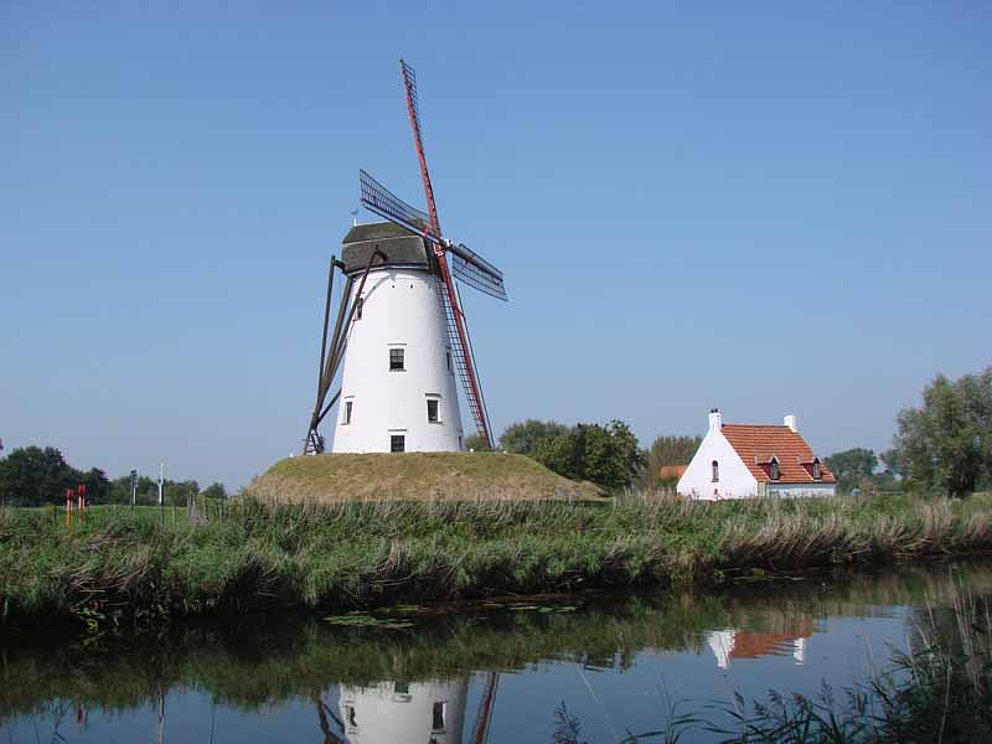 Eine Windmühle in Damme auf einer Wiese unweit eines ruhigen Kanals.