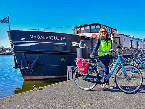 Frau mit Fahrrad steht vor einem Flussschiff