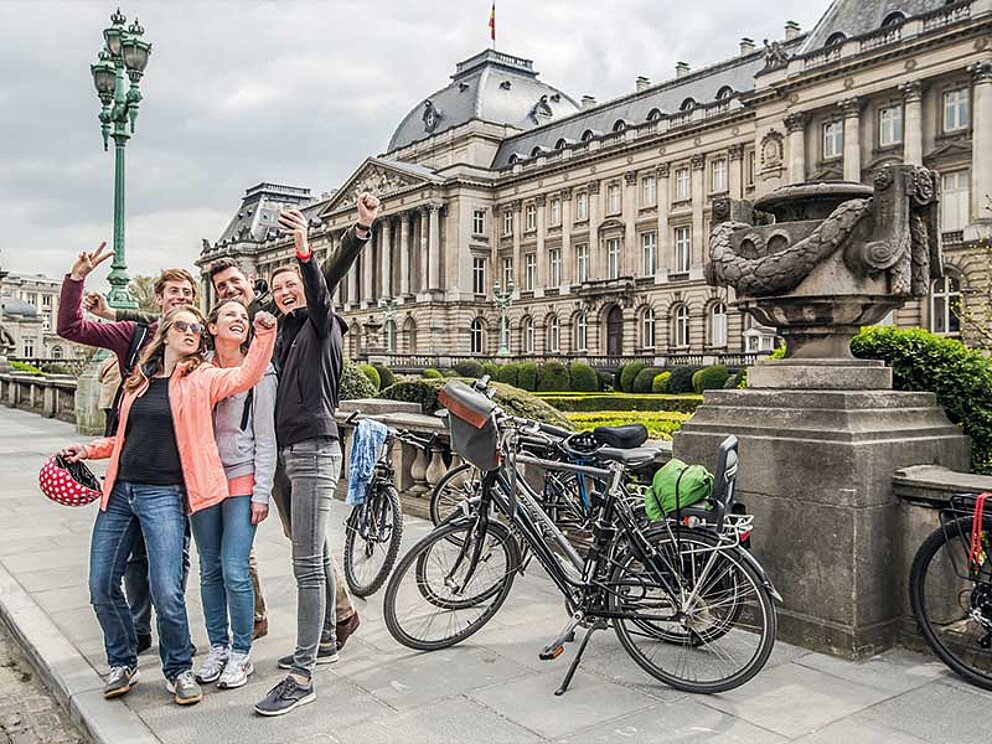 Eine Gruppe junger Menschen mit Trekkingrädern vor einem prächtigen historischen Gebäude in Brüssel, Belgien.