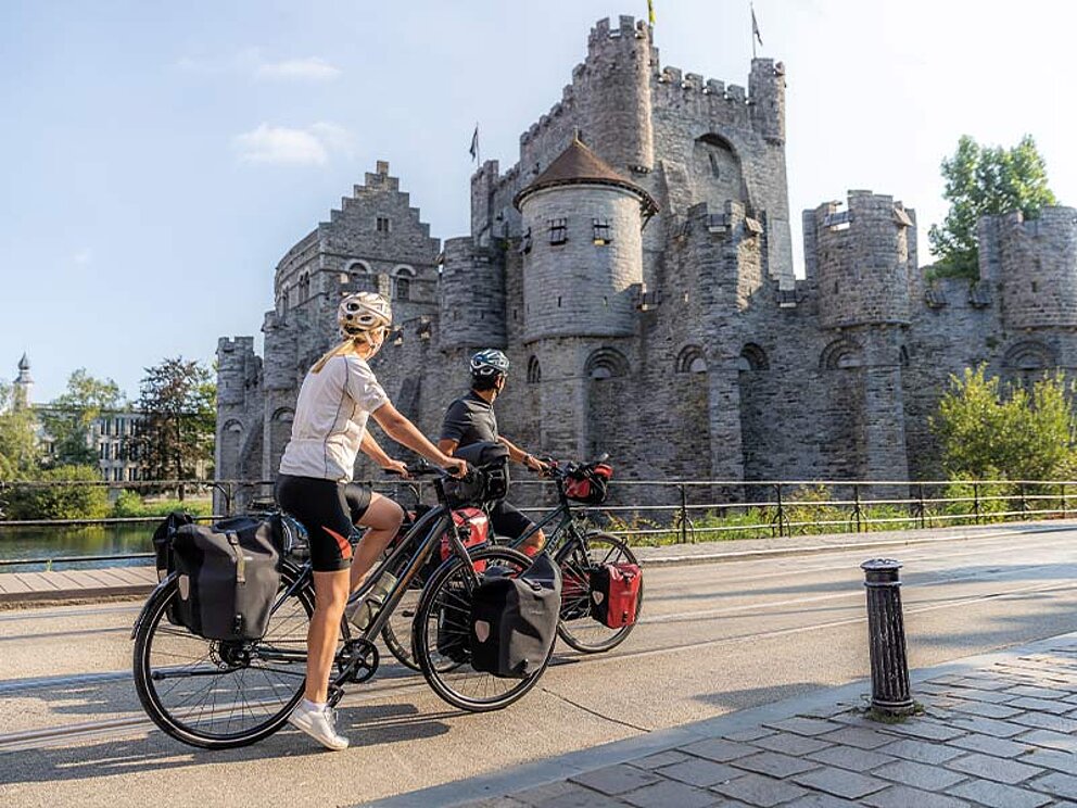 Zwei Radfahrer mit vollgepackten Trekkingrädern und Radtaschen vor der mittelalterlichen Burg Gravensteen in Gent, Belgien.