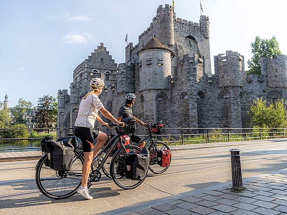 Zwei Radfahrer mit vollgepackten Trekkingrädern und Radtaschen vor der mittelalterlichen Burg Gravensteen in Gent, Belgien.