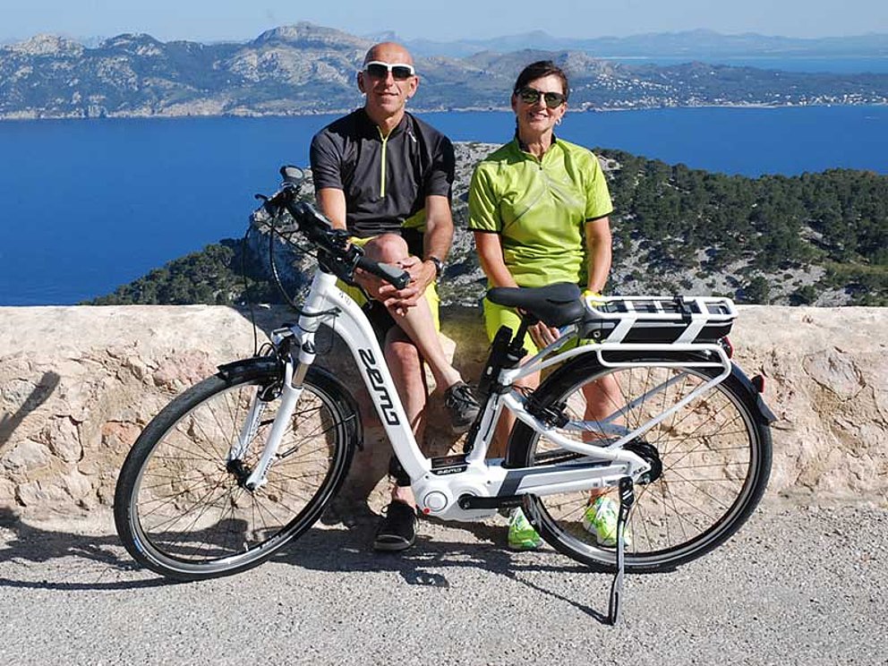 Radfahrer-Paar sitzt auf Steinmauer vor Meer auf Mallorca