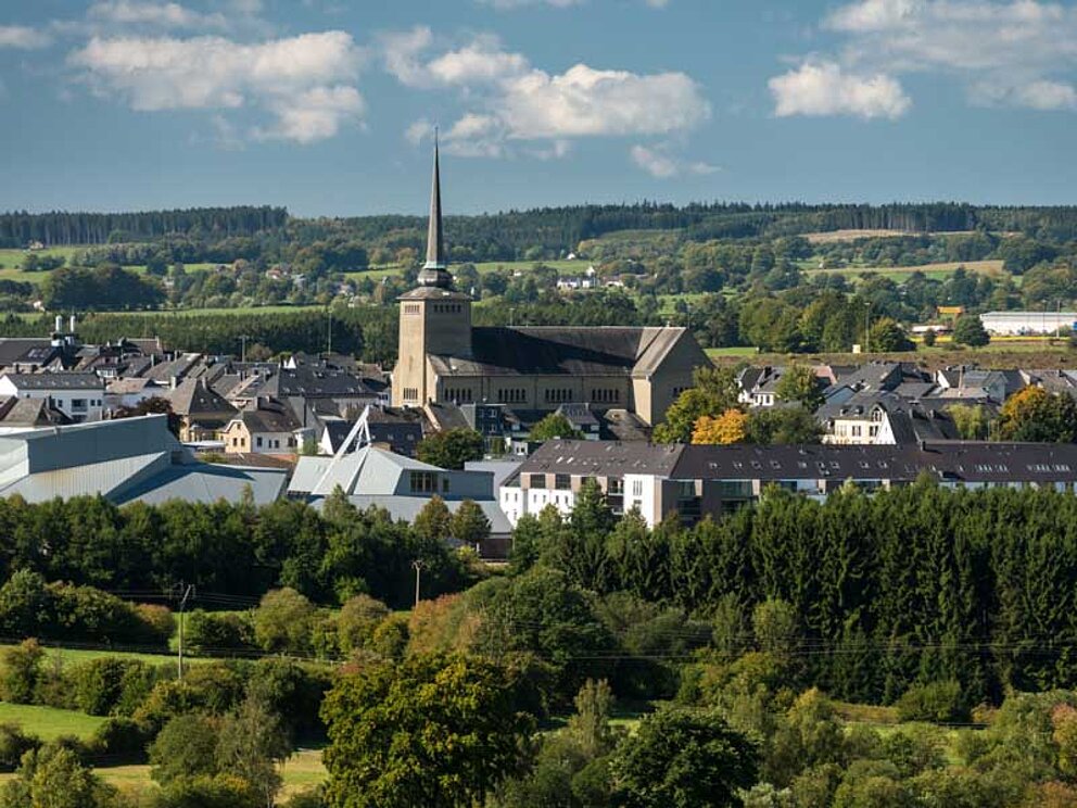 Idyllisches Dorf mit Kirche und Häusern umgeben von Hügeln mit Wäldern und Wiesen