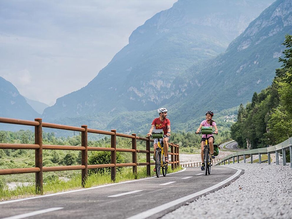 2 Radfahrer am asphaltierten Radweg, im Hintergrund Berge