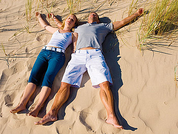 Junges Paar im Sand am Strand liegend direkt vor einer Düne