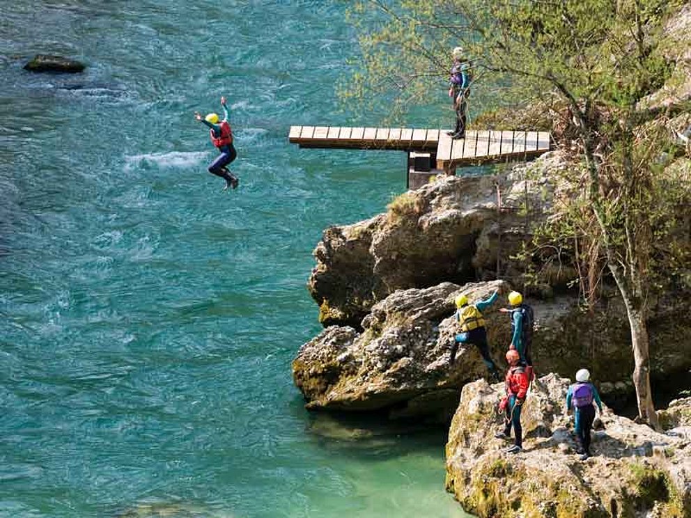 Sportler in Neoprenanzügen springen vom Felsen in einen Gebirgsfluss