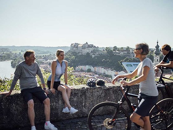 cyclists sitting on a small wall, River Inn and village of Burghausen in the back