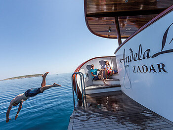 Ein Mann springt ins Meer von der Badeplattform am Heck der Andela Lora