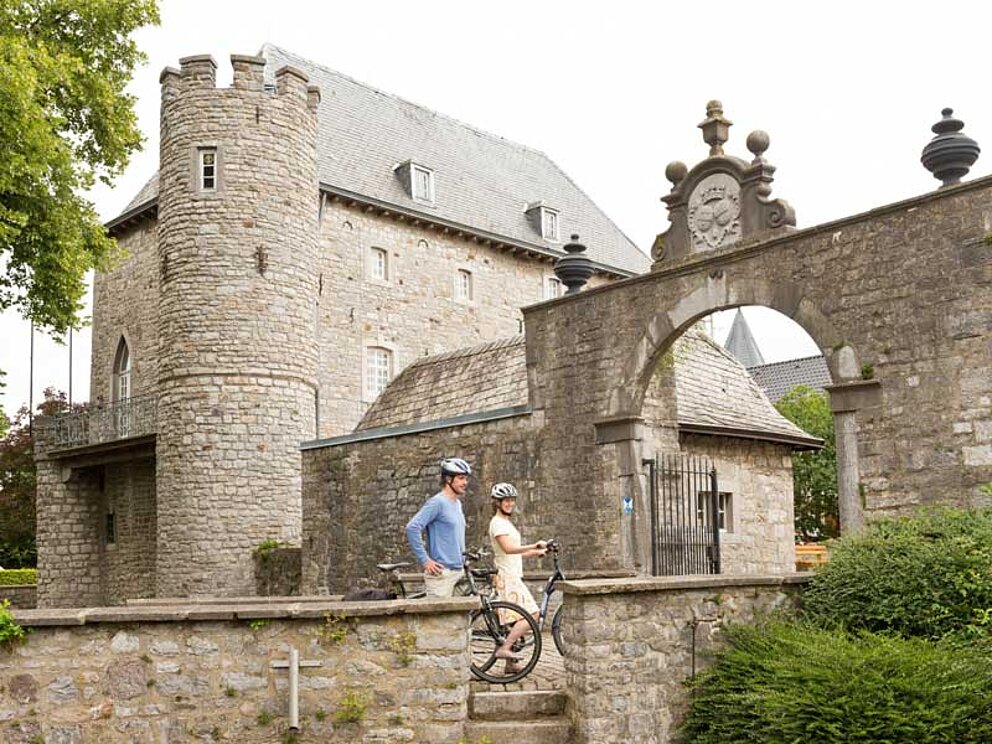 2 Radfahrer vor dem steinernen Burgtor von Burg Raeren.