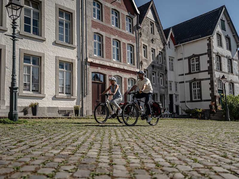 Kopfsteinpflaster in Kornelimünster. 2 Radfahrer vor historischen Gebäuden