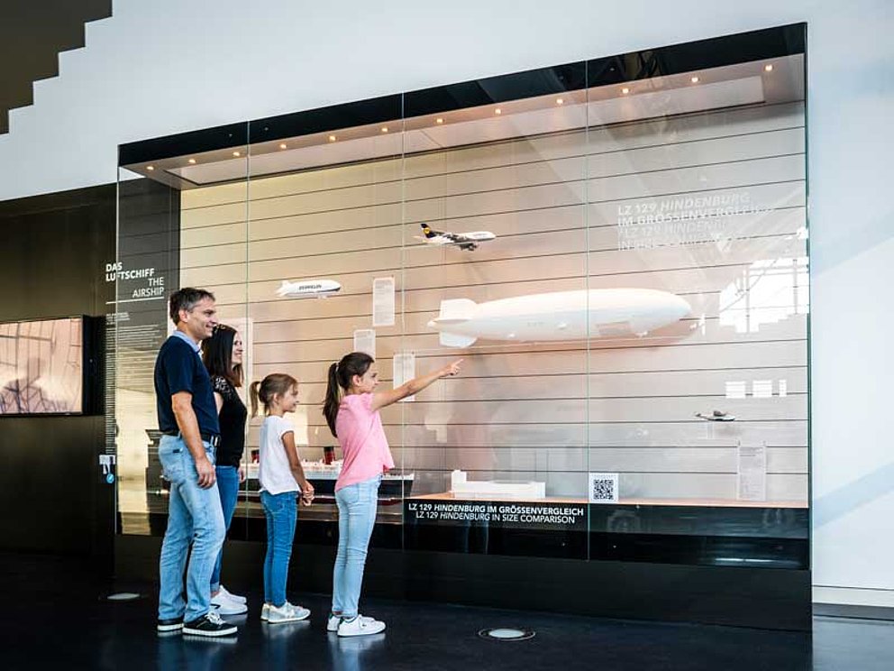 Eltern und zwei Mädchen bestaunen ein Zeppelinmodell