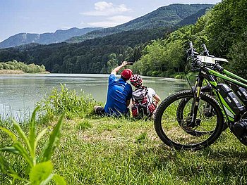 Radfahrer-Paar sitzt am Ufer des Ossiachersees