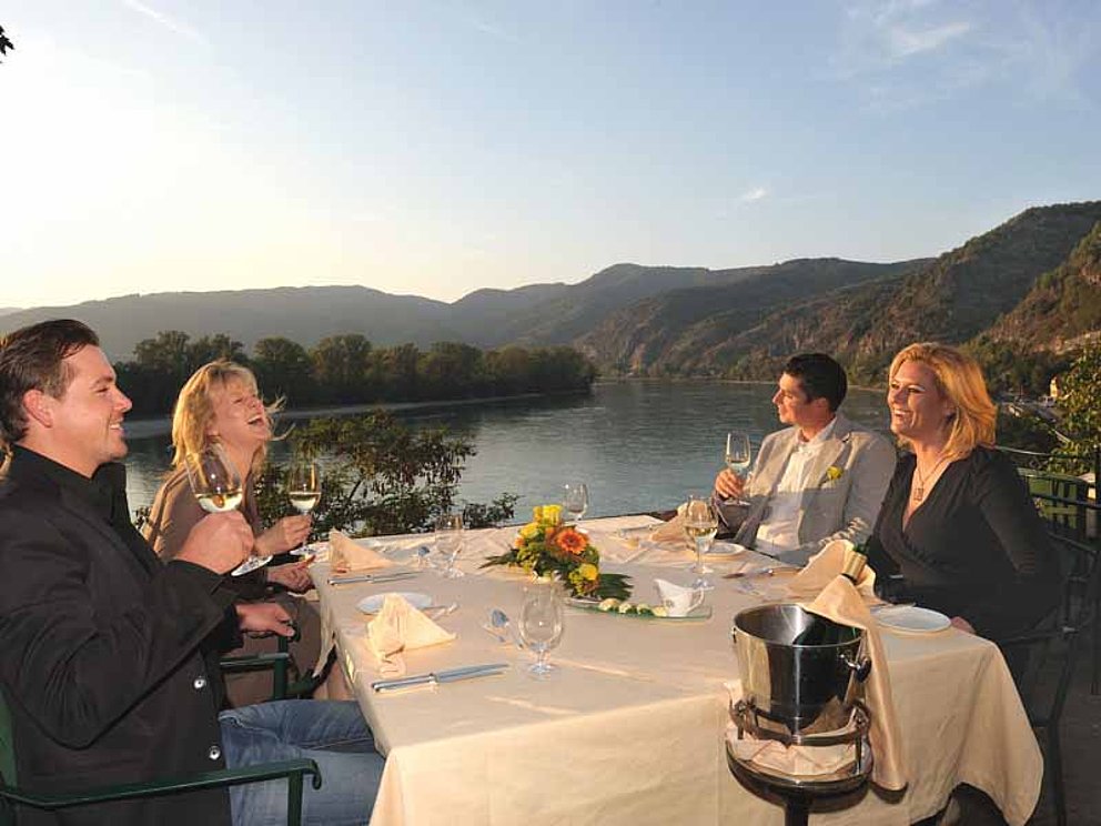 4 Personen genießen das Abendessen bei untergehender Sonne auf der Hotelterrasse von Hotel Schloss Dürnstein in der Wachau.