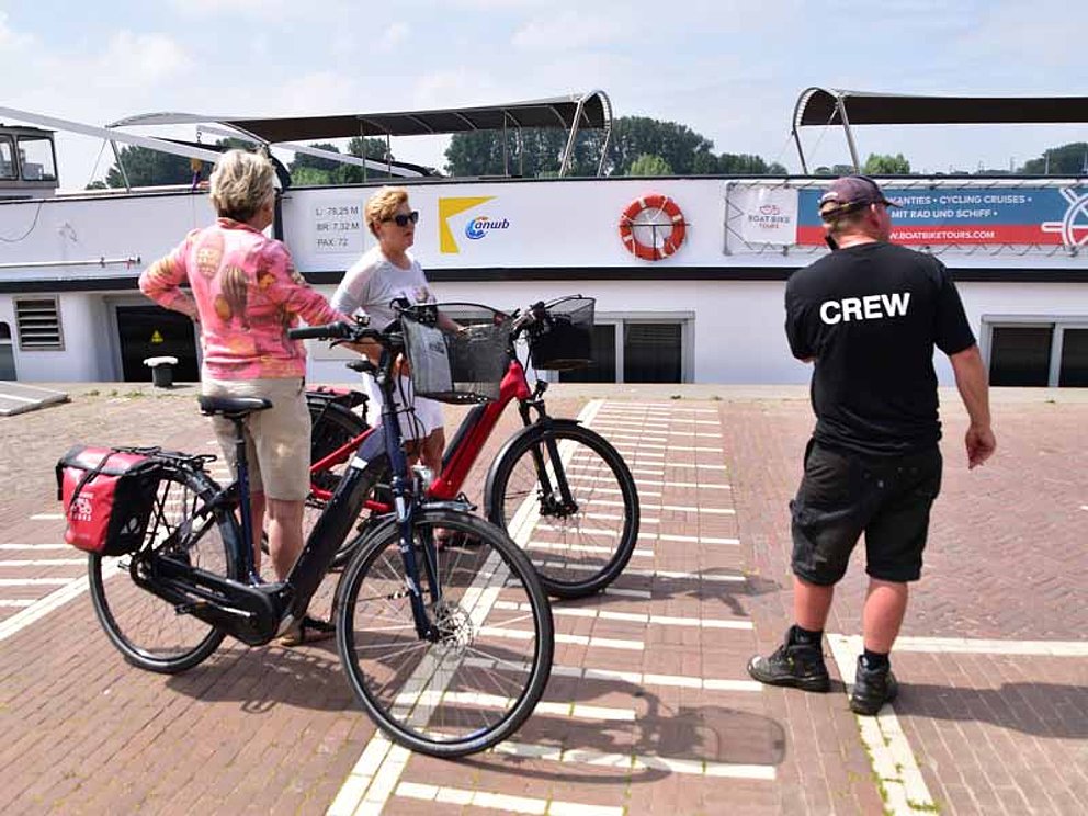 2 Damen mit Fahrrädern und ein Crewmitglied stehen am Pier vor dem Flussschiff