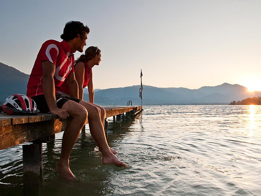 2 Personen sitzen am Steg am Wolfgangsee und lassen die Füße im See baumeln