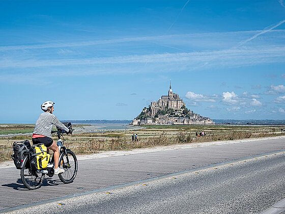 ein Radfahrer auf einem asphaltierten Radweg, im Hintergrund der Mt. St. Michel