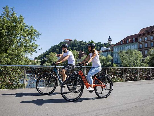 Mann und Frau radeln über eine Brücke, an deren Geländer Liebesschlösser angebracht sind.