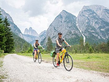 2 Radfahrer am Schotterweg, im Hintergrund Berge